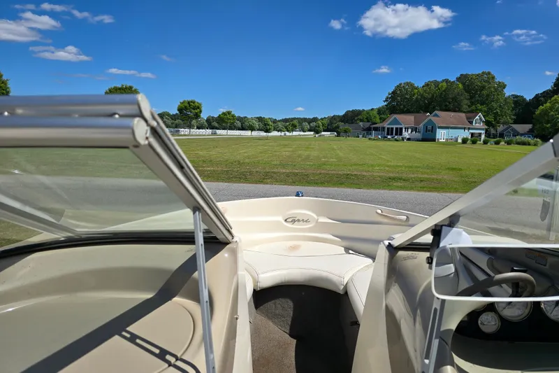 Slide: The Image of 1999 Bayliner 1850 Capri SS boat interior with open windshield, parked near grassy field and houses. - 17