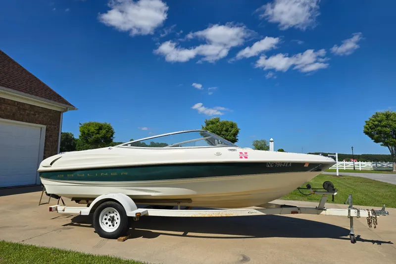 Slide: The Image of 1999 Bayliner 1850 Capri SS boat on trailer, parked in driveway under clear blue sky. - 30