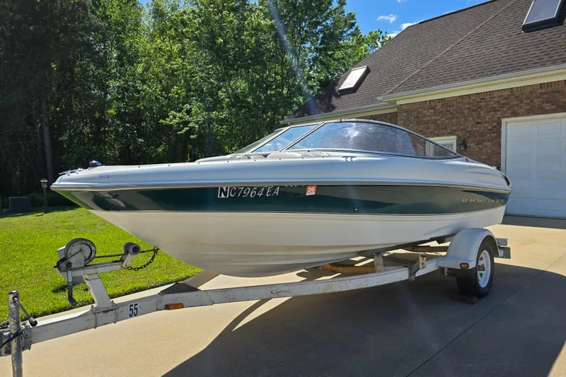Slide: The Image of 1999 Bayliner 1850 Capri SS boat on trailer, parked in driveway, surrounded by greenery. - 6