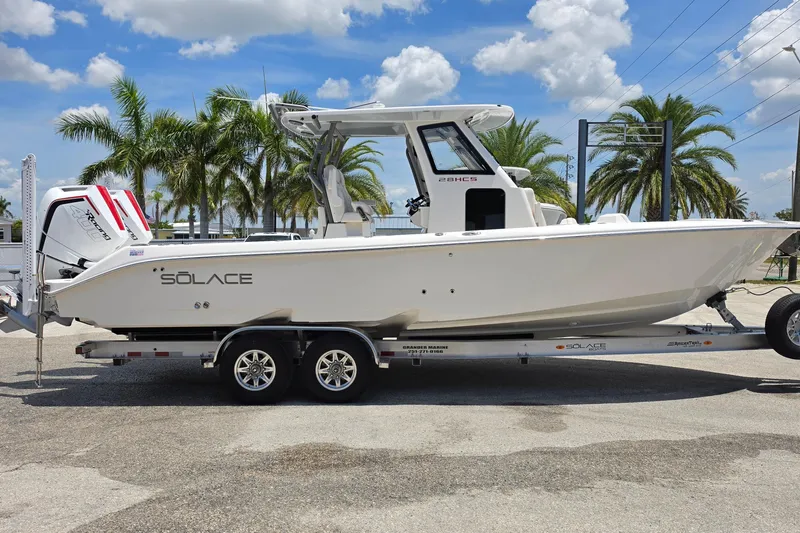 Slide: The Image of 2026 Solace 28HCS boat on trailer, parked under palm trees, clear sky background. - 1