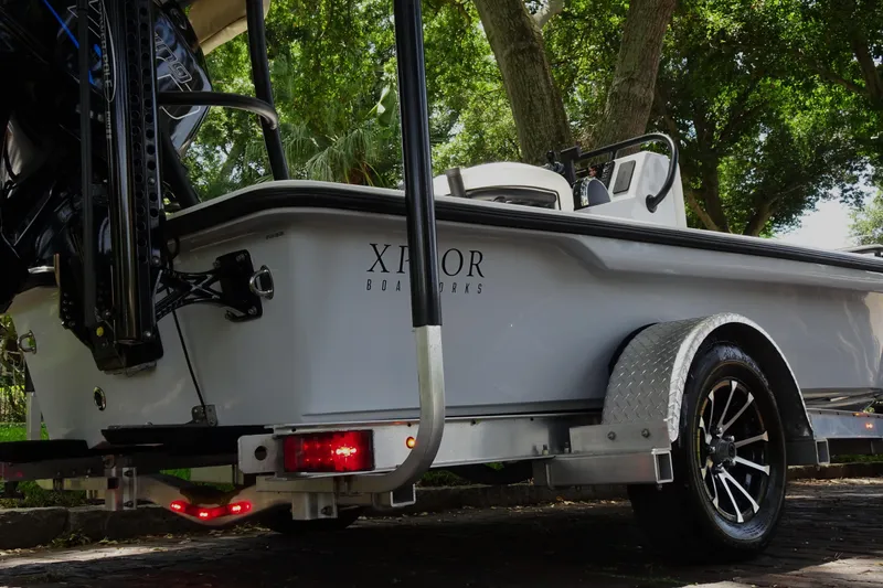 Slide: The Image of 2024 Xplor X18 Delta D18 boat on trailer, surrounded by trees. - 8