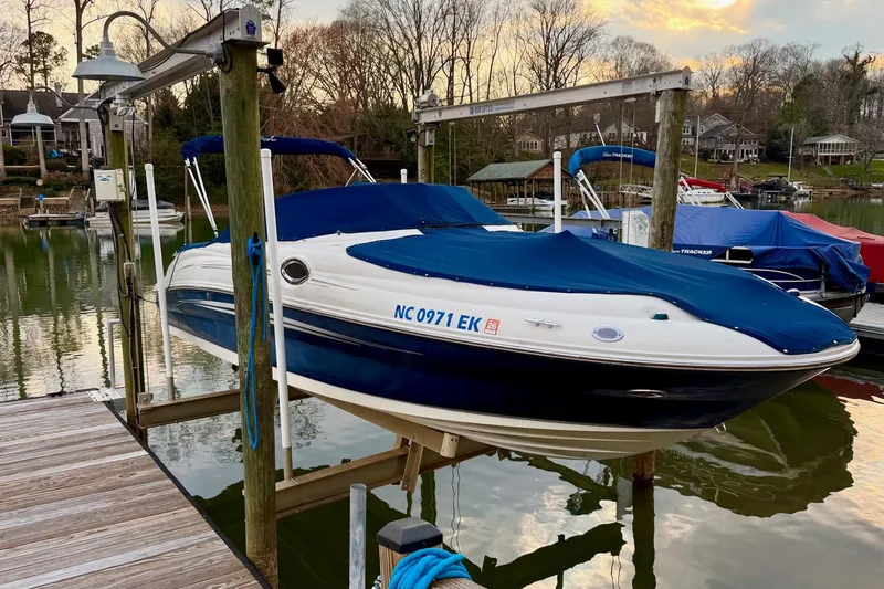 The Image of 2008 Sea Ray 240 Sundeck boat docked with blue cover at a serene lakeside. - 0