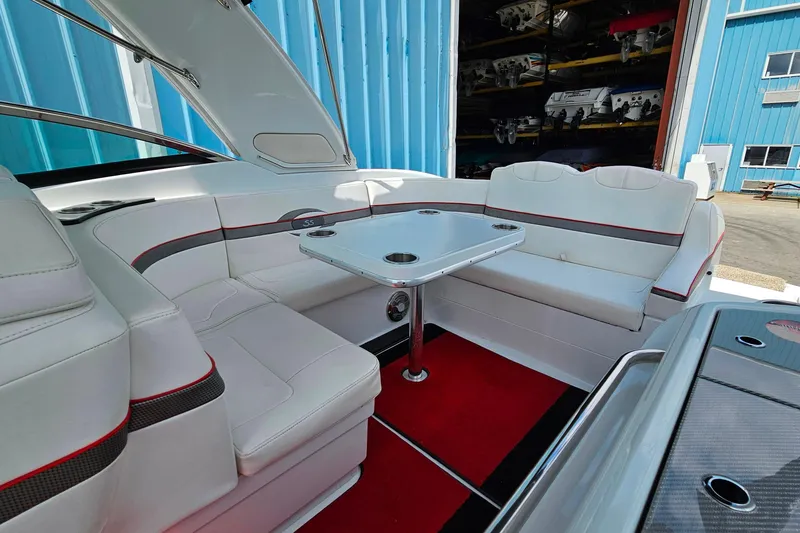 Slide: The Image of 2013 Formula 310 FX5 boat interior with white seating and table, docked near blue warehouse. - 24