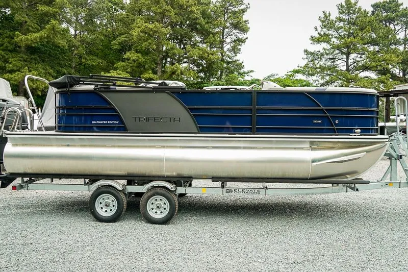 Slide: The Image of 2026 Trifecta LE 22RF pontoon boat on trailer, surrounded by trees. - 3