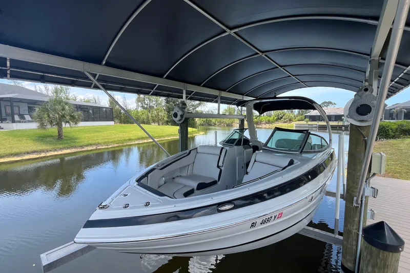 Slide: The Image of 2022 Crownline 260 XSS boat docked under a canopy on a serene waterfront. - 2