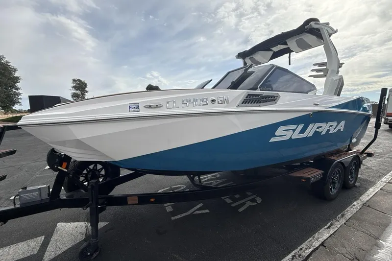 The Image of 2024 Supra SA 550 boat on trailer, blue and white design, parked outdoors. - 1
