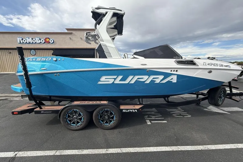 Slide: The Image of 2024 Supra SA 550 boat in blue and white on a trailer, parked outdoors. - 6