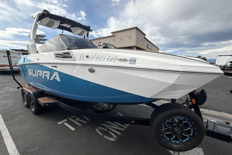 Slide: The Image of 2024 Supra SA 550 boat on trailer, blue and white design, parked outdoors. - 7