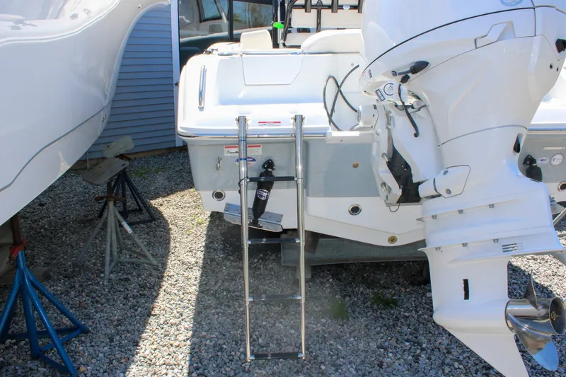 Slide: The Image of 2026 Sea Hunt Ultra 219 boat with ladder and outboard motor on gravel. - 12