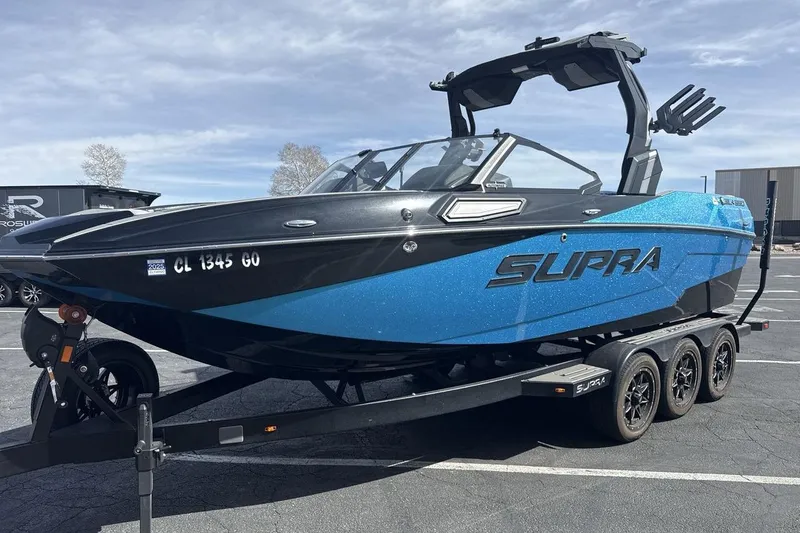 The Image of 2024 Supra SL 550 boat on trailer in parking lot, blue and black design. - 1