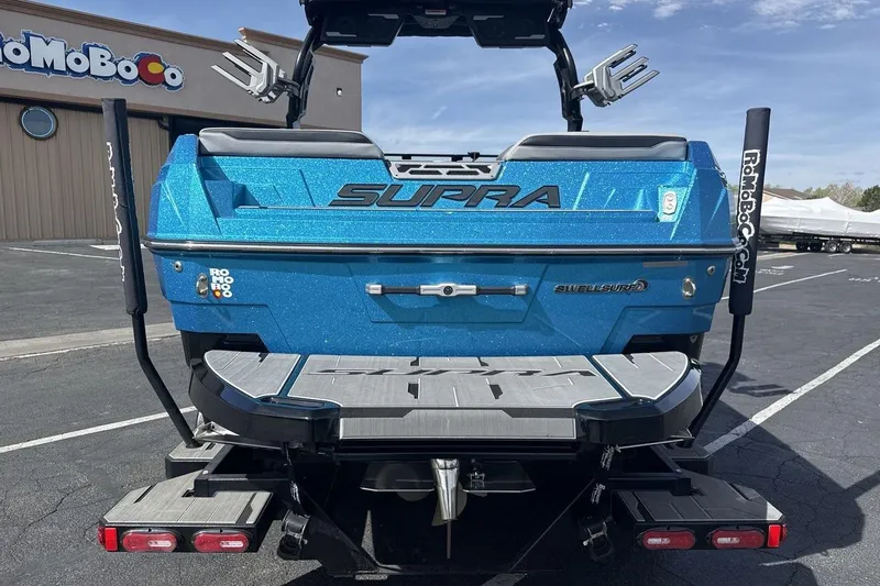 Slide: The Image of 2024 Supra SL 550 boat in vibrant blue, rear view with swim platform and surf equipment. - 4