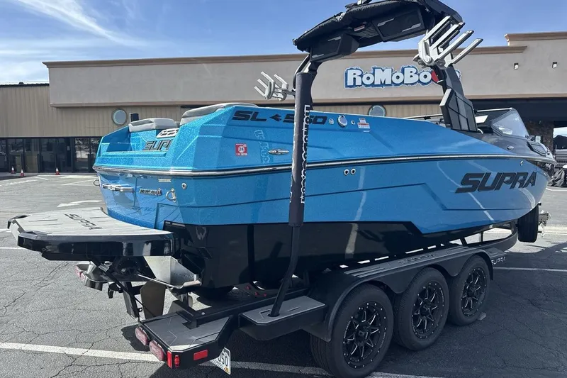 Slide: The Image of 2024 Supra SL 550 boat in vibrant blue on a trailer, parked outside a building. - 5