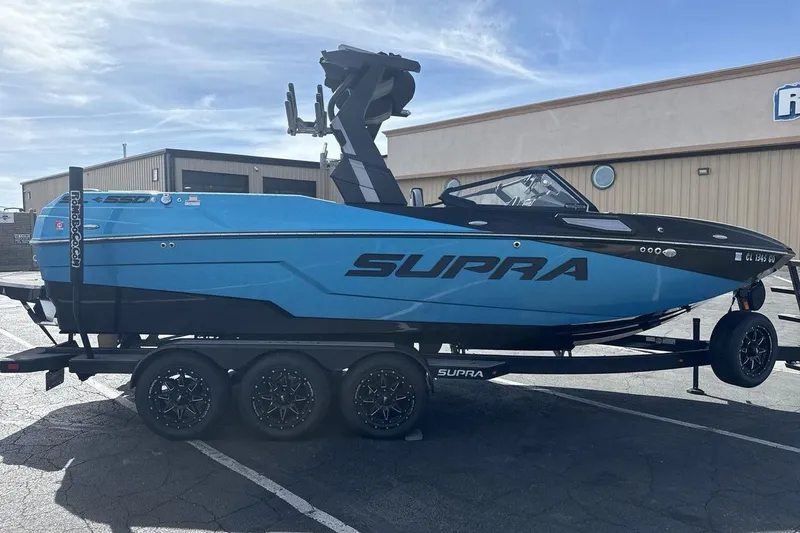 Slide: The Image of 2024 Supra SL 550 boat in blue on a trailer, parked outdoors. - 6
