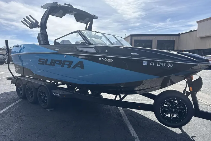 Slide: The Image of 2024 Supra SL 550 boat on trailer, blue and black design, parked outdoors. - 7