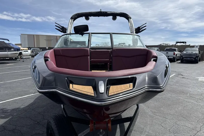 Slide: The Image of 2023 MasterCraft NXT22 boat with maroon interior, parked outdoors under a blue sky. - 8