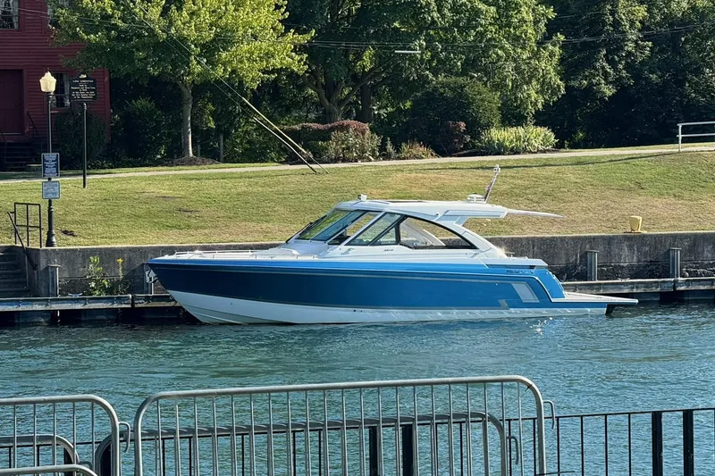 Slide: The Image of 2022 Formula 380 Super Sport Crossover I/O boat docked by a grassy shoreline. - 2