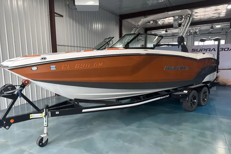 The Image of 2021 MasterCraft NXT24 boat in showroom, orange and white, on trailer. - 1