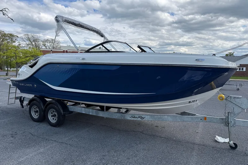 The Image of 2026 Bayliner D22I boat on trailer, blue and white design, parked outdoors under cloudy sky. - 0