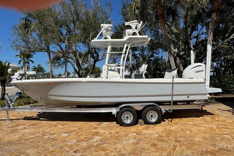 The Image of 2020 Robalo 246 Cayman SD boat on trailer, parked outdoors with trees in background. - 0