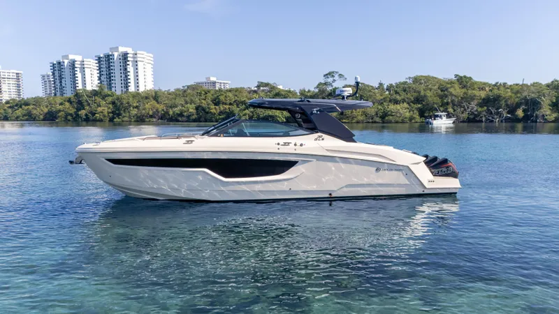 Slide: The Image of 2021 Cruisers Yachts 38 GLS OB 450R on calm water, with cityscape and trees in background. - 7