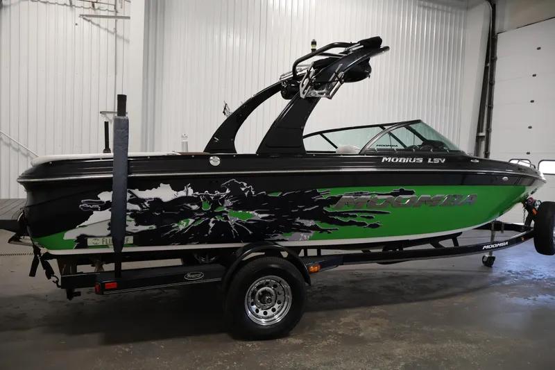 Slide: The Image of 2011 Moomba Mobius LSV boat with green and black design in a garage setting. - 3