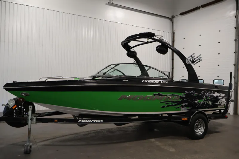 Slide: The Image of 2011 Moomba Mobius LSV boat with green and black design in a garage setting. - 7