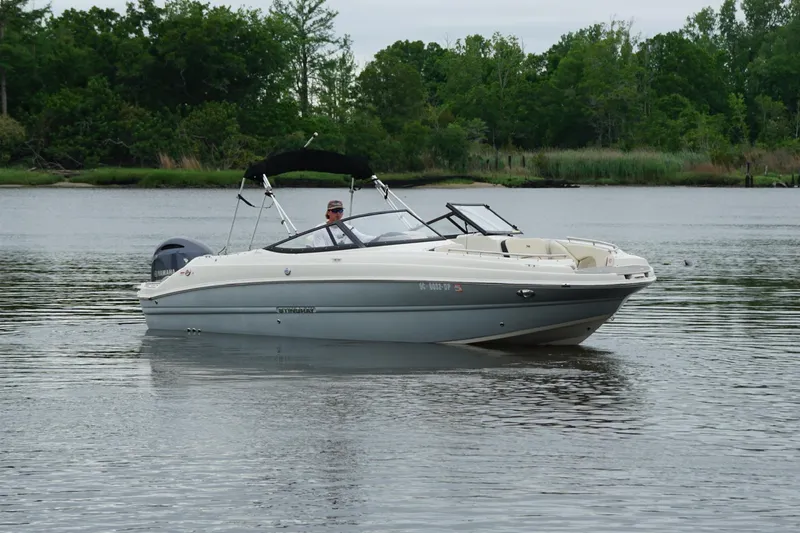 Slide: The Image of 2021 Stingray 231 DC boat cruising on a calm lake with lush greenery. - 16