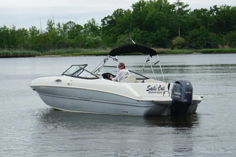Slide: The Image of 2021 Stingray 231 DC boat cruising on a calm lake with lush greenery. - 18