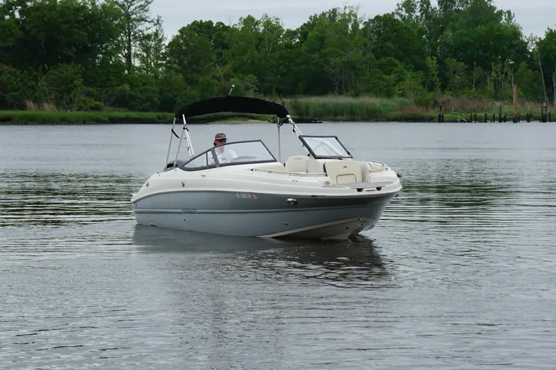Slide: The Image of 2021 Stingray 231 DC boat cruising on a calm lake with trees in the background. - 19