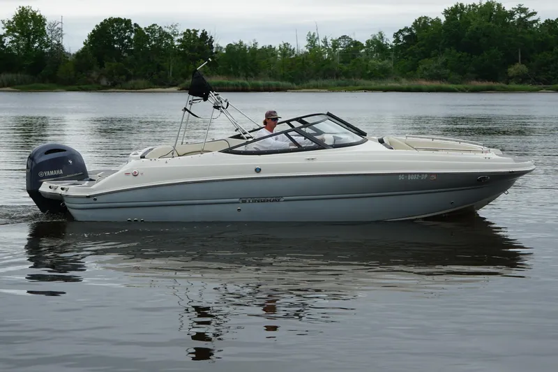 Slide: The Image of 2021 Stingray 231 DC boat cruising on a calm lake with Yamaha outboard motor. - 20