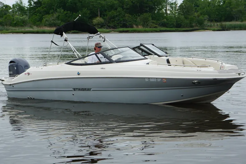 Slide: The Image of 2021 Stingray 231 DC boat cruising on a calm lake with lush greenery in the background. - 4