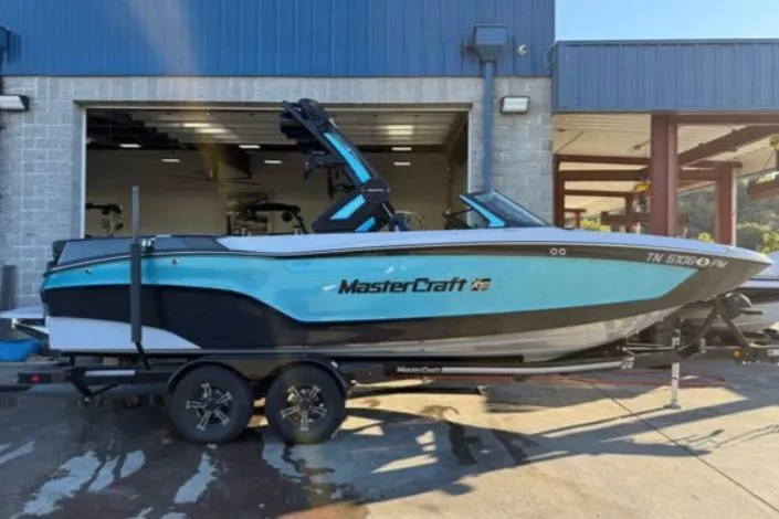 The Image of 2023 MasterCraft XT24 boat on trailer outside a garage. - 0