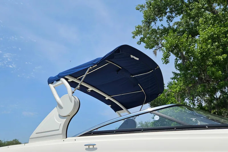 Slide: The Image of 2018 Sea Ray SLX 230 boat with blue canopy against clear sky and trees. - 2