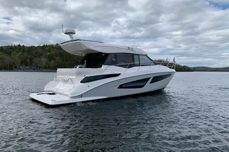 Slide: The Image of 2019 Regal 42 Grande Coupe yacht on a serene lake under cloudy skies. - 2