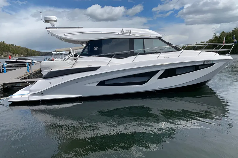 Slide: The Image of 2019 Regal 42 Grande Coupe yacht docked on calm water under a cloudy sky. - 38