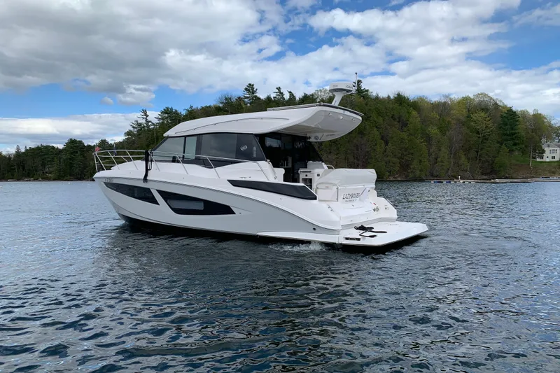 Slide: The Image of 2019 Regal 42 Grande Coupe yacht cruising on a serene lake with forested shoreline. - 4
