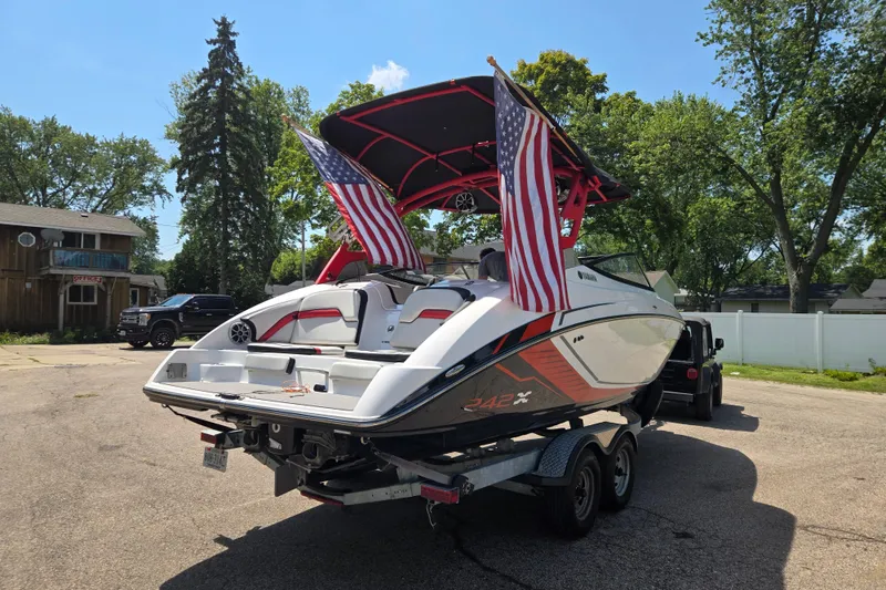 Slide: The Image of 2018 Yamaha Boats 242X on trailer with American flags, parked outdoors. - 2