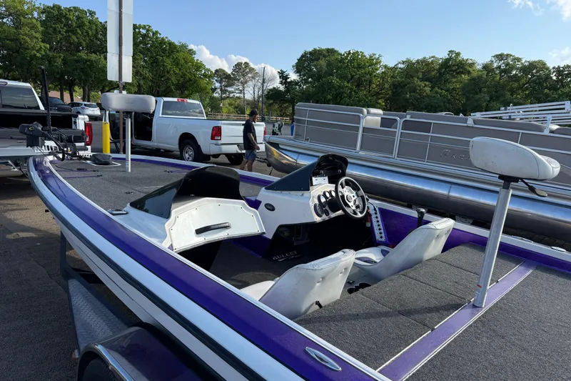 Slide: The Image of 2002 Bullet 21XDC boat with purple accents, parked near trucks and trees. - 17