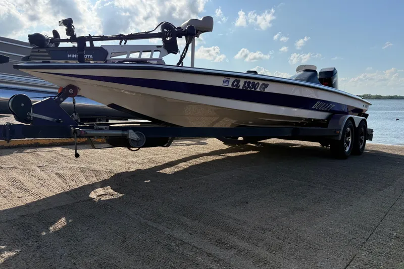 Slide: The Image of 2002 Bullet 21XDC boat on trailer by the water, under a partly cloudy sky. - 21