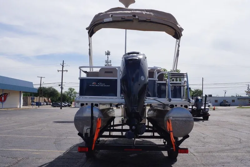Slide: The Image of 2025 Sun Tracker Bass Buggy 18 DLX pontoon boat with canopy and motor, parked outdoors. - 14