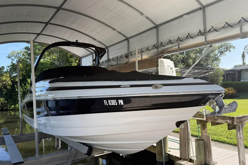 The Image of 2013 Crownline 285 SS boat under a canopy, docked near a lush green landscape. - 1