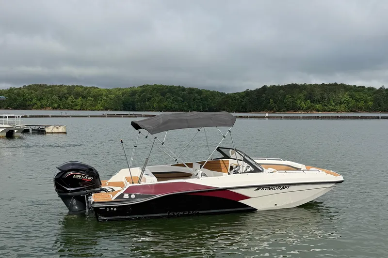 Slide: The Image of 2023 Starcraft SVX 210 DC OB boat on a calm lake with lush green shoreline. - 13