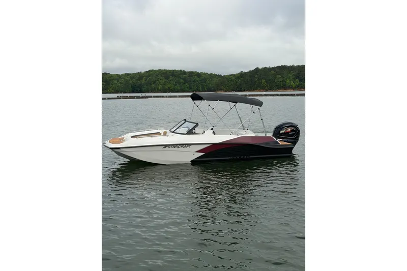 Slide: The Image of 2023 Starcraft SVX 210 DC OB boat on a calm lake with lush green shoreline. - 16