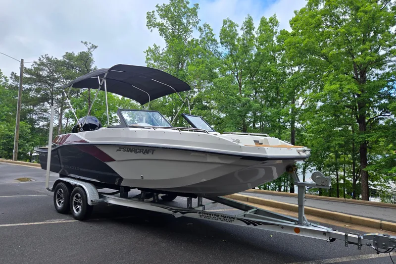 Slide: The Image of 2023 Starcraft SVX 210 DC OB boat on trailer, parked near lush green trees. - 18