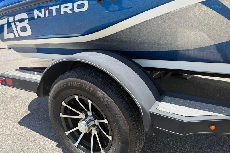 Slide: The Image of 2017 Nitro Z18 boat trailer with black wheel and fender, parked on asphalt. - 2