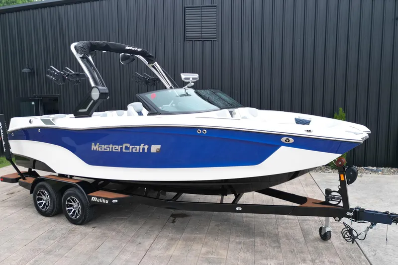 Slide: The Image of 2023 MasterCraft XT22 boat on trailer, blue and white design, parked outdoors. - 16