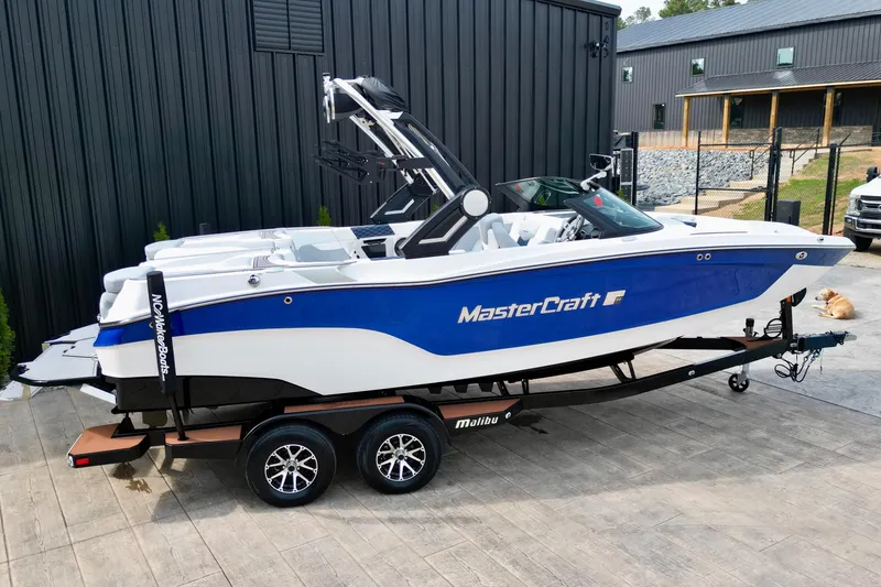 Slide: The Image of 2023 MasterCraft XT22 boat on trailer, blue and white design, parked outdoors. - 3