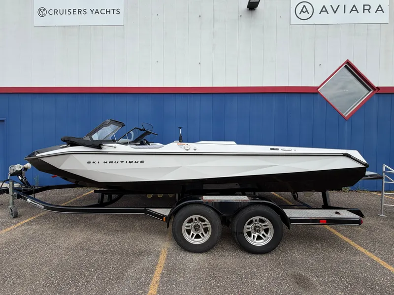 Slide: The Image of A white 2027 Ski Nautique boat on a trailer in front of a building. - 0