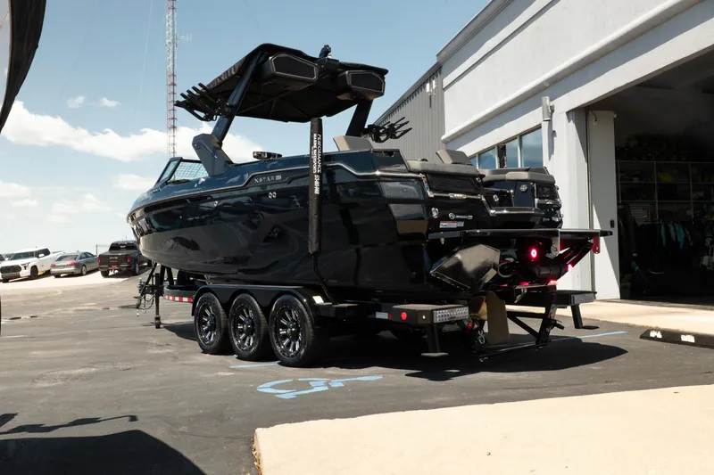 Slide: The Image of 2026 MasterCraft XStar 25 boat on trailer, parked outside a building under clear skies. - 10