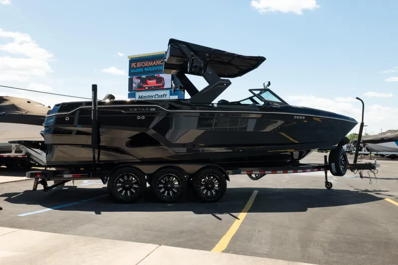 Slide: The Image of 2026 MasterCraft XStar 25 boat on trailer at dealership under clear sky. - 16